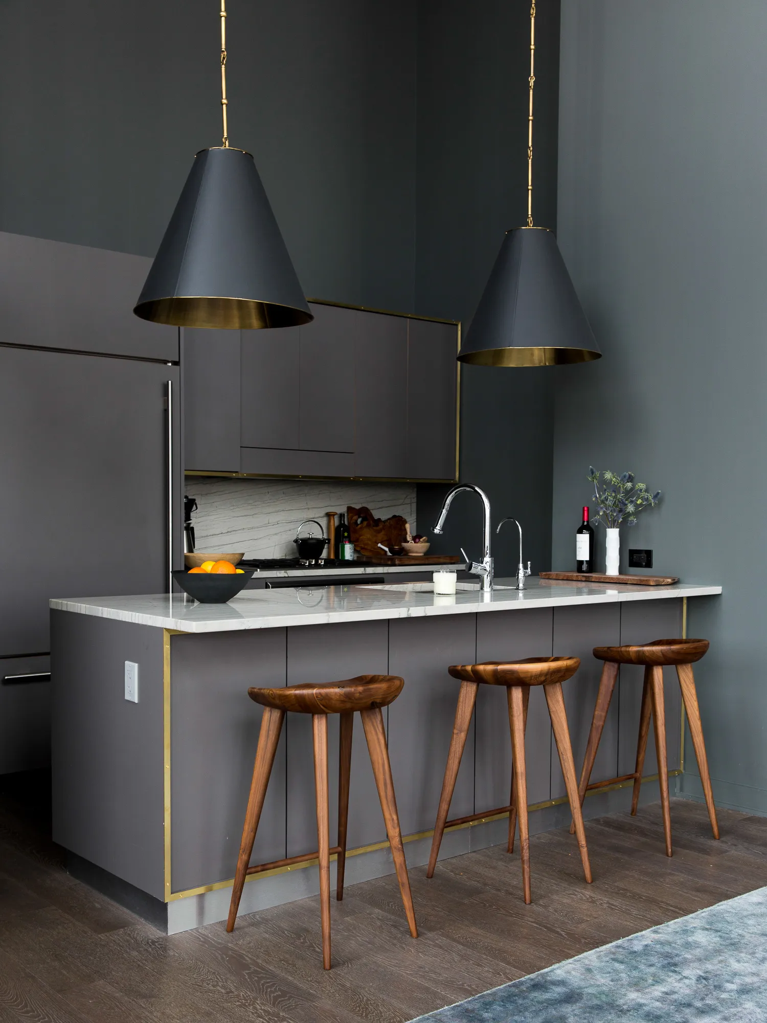 Charcoal kitchen with brass-lined pendants and walnut stools